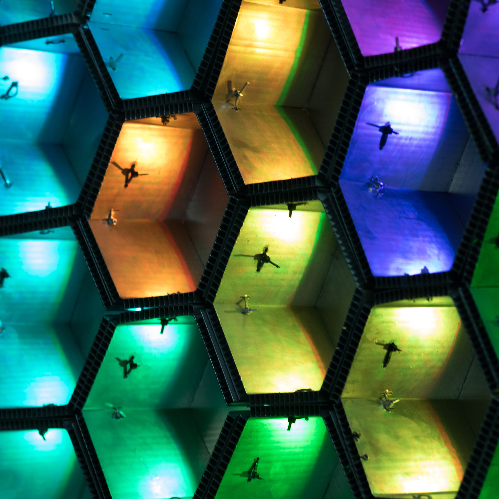 Close-up of HEXTIC's hexagonal prisms lit in a rainbow gradient, with rippled reflections across their faces