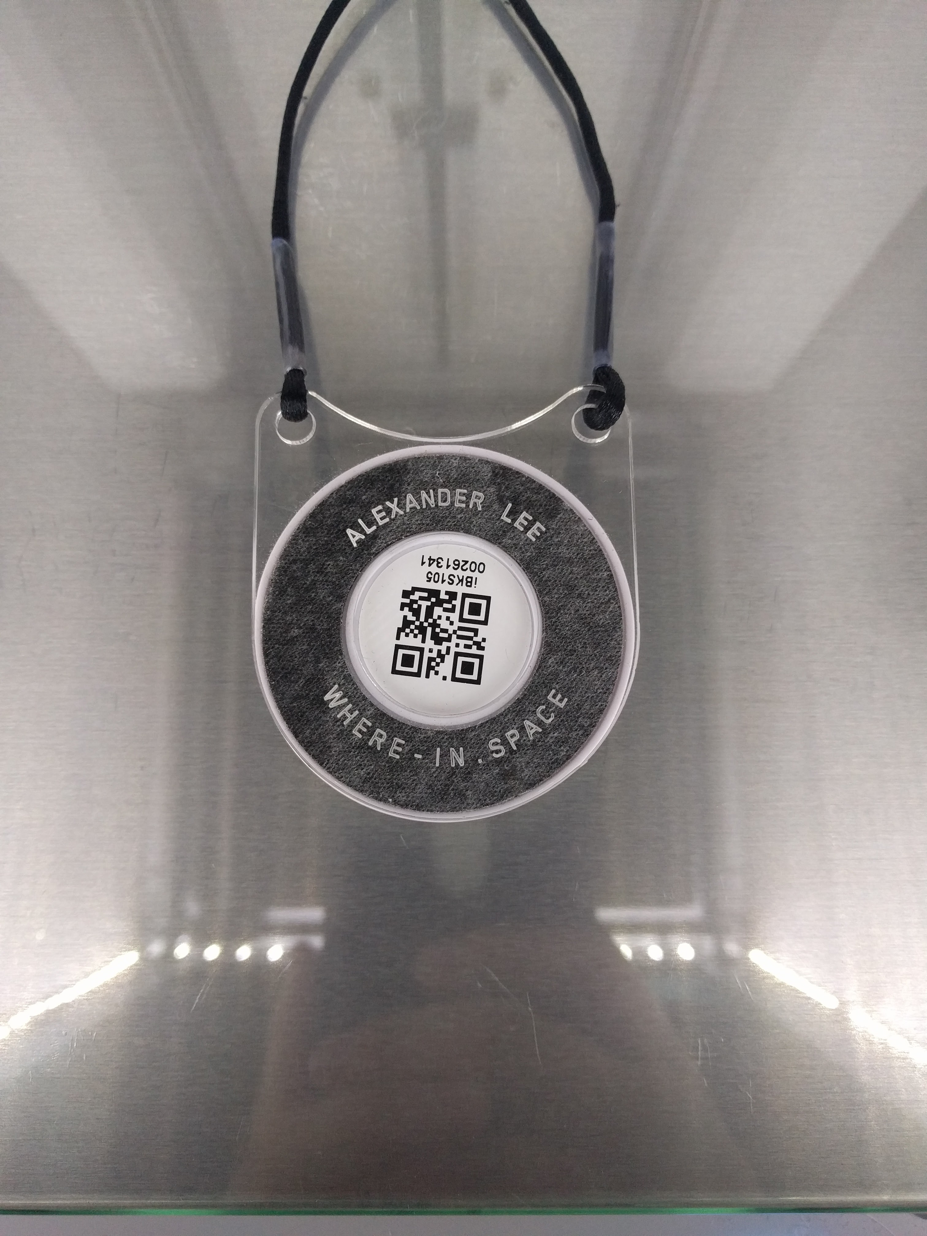 A laser-etched acrylic beacon tag reading "Alexander Lee · WHERE-IN SPACE" with a QR code, sitting in a 3D printer
